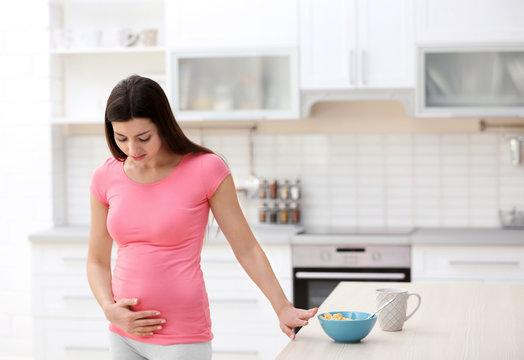 Beautiful woman experiencing signs of pregnancy in kitchen