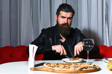 Bearded man eating pizza with knife and fork