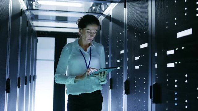 Female Server Technician Walking in Data Center Corridor with Rows of Rack Servers. She's Running Diagnostics on Her Tablet Computer Shot on RED EPIC-W 8K Helium Cinema Camera.