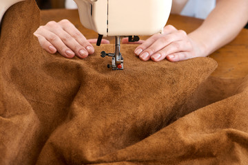Female tailor threading leather material on sewing machine