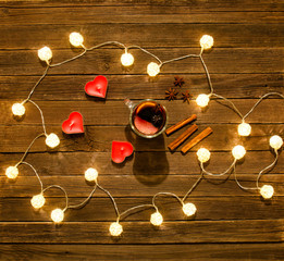 Top view of mulled wine with spices, candles in the shape of a heart, cinnamon sticks, star anise on a wooden table. Garland of lanterns.