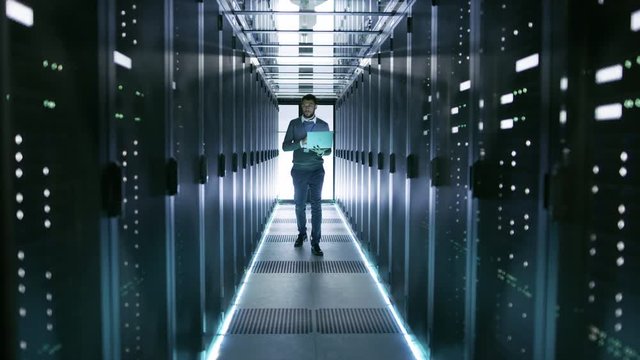 Male Server Engineer Walks with Laptop Through Working Data Center Full of Rack Servers. Shot on RED EPIC-W 8K Helium Cinema Camera.