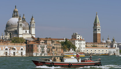 Fototapeta premium A boat with a man sitting on it crosses the Venetian lagoon with in the background the Campanile di San Marco and the Basilica della Salute, Venice, Italy