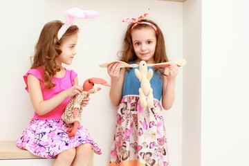 Cute little girls with bunny ears and cuddly toy stand near the white wall