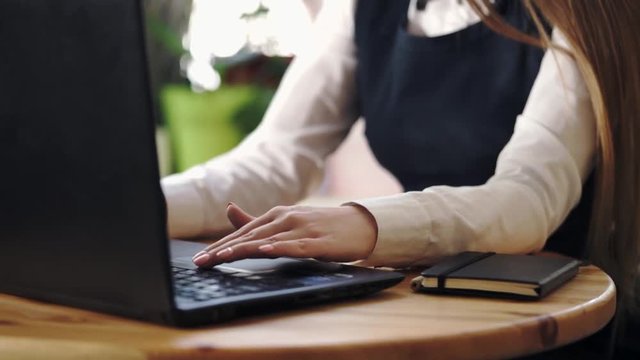 Close up shot of a young woman with manicure typing text on a laptop. There is a notebook on the table, this girl is a manager or a businesswoman.