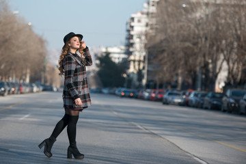 Fashion teen in city wear coat and hat walking in profile at the middle of the highway