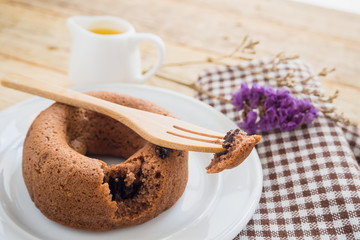 Chocolate donut scoop out with a wooden fork on chocolate donut in dish with jug of honey on wooden background.