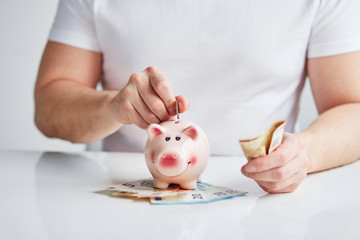 Obraz na płótnie Canvas Man putting coin into small piggy bank