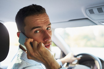 Young businessman in car with phone and looking back