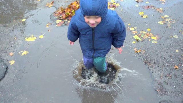 Happy little boy jumping in muddy puddle, slow motion