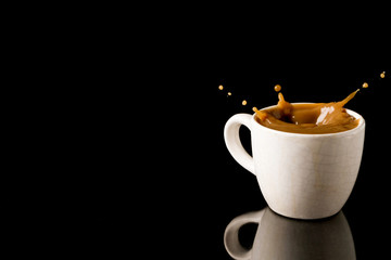 Cup of splashing coffee on black background. Free space for text