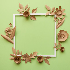 square frame with craft paper flowers on the green background. Flat lay. Nature concept