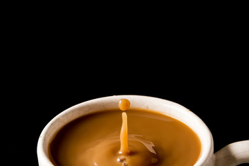 A cup of coffee with a drop on black background.