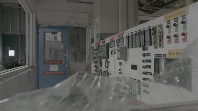 A tilt and rack focus from the shattered glass of a broken window to the interior of a control room in an abandoned factory.