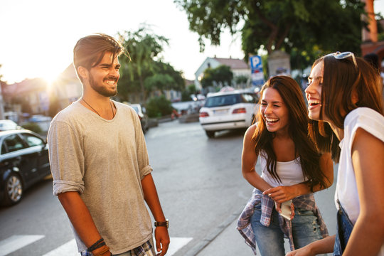 A vibrant group of young friends gathers at the city street, enjoying each other's company, laughter, and the lively atmosphere of their urban hangout.