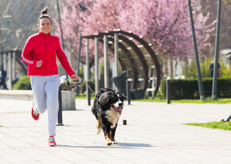 Naklejka na ściany i meble Young pretty girl running outdoor with her Bernese Mountain dog