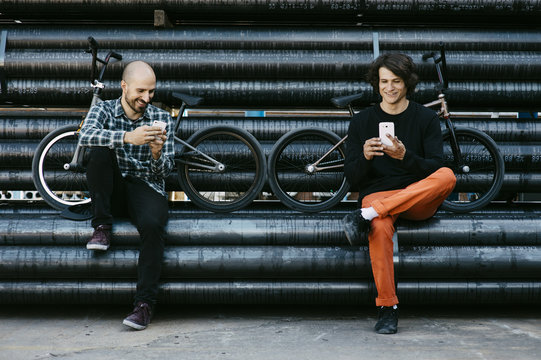 Smiling friends using smartphone while sitting on metal pipe