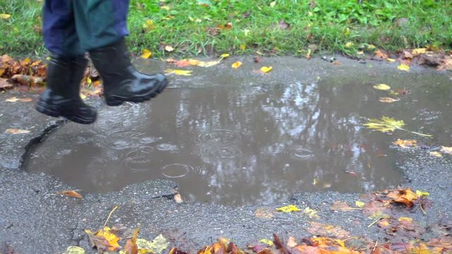 Little boy jumping in muddy puddle, slow motion