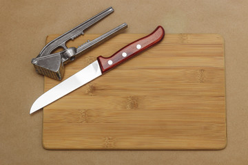 Kitchen knife and garlic press on cutting board with copyspace.
