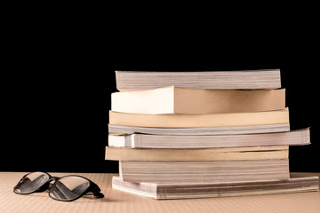 Stack of books and eyeglasses on wooden table, Black background
