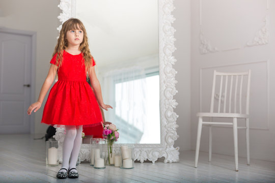 little girl in a red dress wistful glance at the mirror