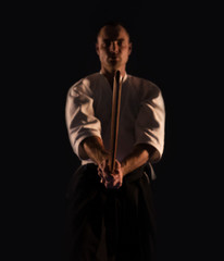 Fototapeta na wymiar Aikido practicer (Aikidoka) with a training wooden sword (boken) dark dojo photo