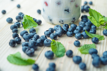 Rustic healthy breakfast with blueberry and yogurt in a glass on a wooden table. Glass of homemade yogurt with ripe berries. Mint leaves with blackberries. Healthy breakfast with vital vitamins.