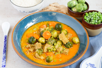 Curry with pork, brussels sprouts and green peas. Blue plate, rice, ginger, green peas.