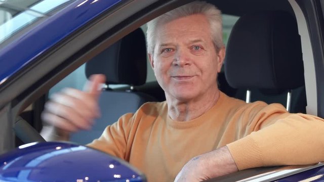 Senior caucasian man looking into the side mirror of the car. Aged male customer sitting inside the vehicle. Close up of attractive gray client showing his thumb up through the window