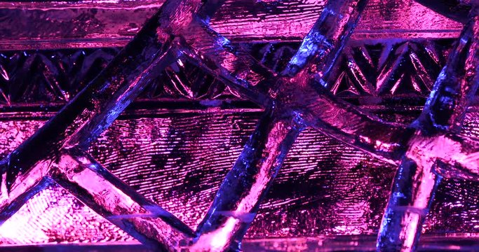 Extreme close up shot of ice carved into a crisscross pattern with pink lighting