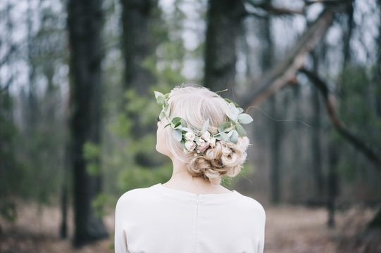 Beautiful blond bride with a floral head band standing back to the camera in the winter forest