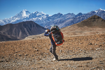 Nepalesischer männlicher Träger, der schwere Lasten im Himalaya, Nepal trägt. Dhaulagiri-Gipfel im Hintergrund.