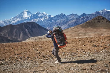 Fotobehang Dhaulagiri Nepalese mannelijke portier die zware lasten in Himalayagebergte, Nepal draagt. Dhaulagiri bergtop op de achtergrond.