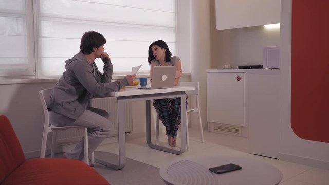 Happy family enjoy breakfast and planning working day. Woman and man owners startup company discussing work in the morning at home. On the table breakfast food and drink, computer. Girlfriend point