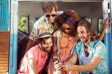 Group of happy friend using mobile phone in campervan