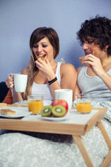 Young happy couple in love having breakfast in bed served over a tray at home. Couple home lifestyle concept.