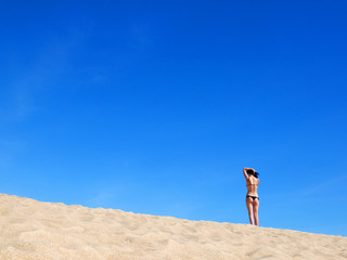 Sexy girl in bikini standing back to back at sandy beach with big blue sky
