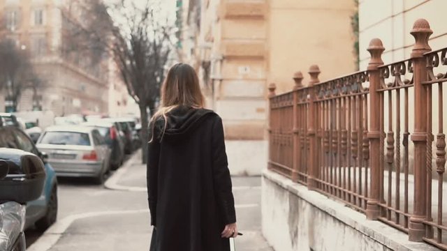 Young woman in black coat walking in the old town part. Back view of the girl exploring the new city. Slow motion.