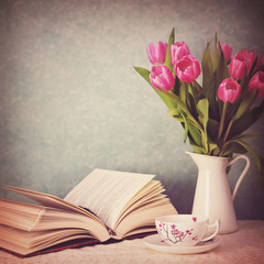Open book, a cup of tea and pink tulips in a vase