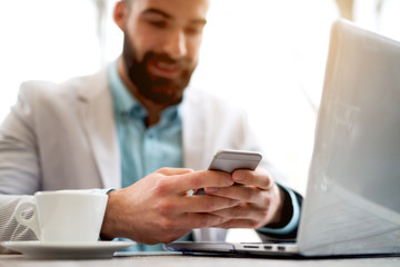 Businessman typing message mobile phone laptop cafe bar office.