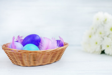 Basket with colored eggs and flowers on wooden background. Concept Happy Easter.