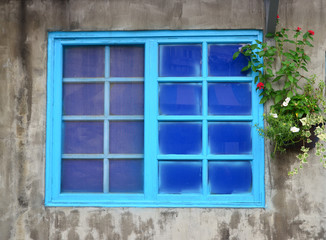 Window on cement wall with blue wooden frames, flower pot hang on the wall.