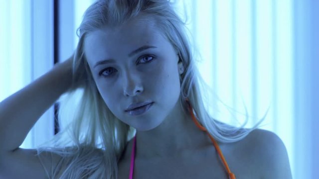 Young woman stand in bathingsuit in solarium and sunbathes in salon