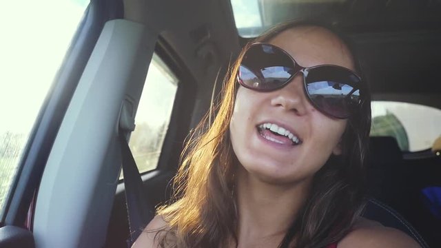 Joyful young woman wears sunglasses sitting in car passenger enjoying rural looking out window on sunny day and singing song in slow motion with beautiful lense flare effects. 1920x1080