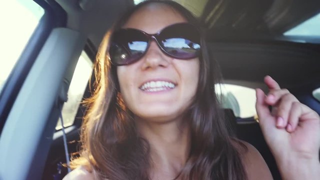 Cheerful young woman wears sunglasses sitting in car passenger and singing song in slow motion with beautiful sun lense flare effects on the background. 1920x1080