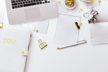 A desktop flatlay scene, with a white and gold planner, laptop, notepad, screwed up balls of paper...