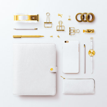 Square Flatlay Scene, With Closed White Organizer, Iphone And Gold Feminine Stationery Accessories. Arranged In A Grid On A Plain White Background.