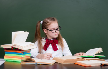 Young girl reading a books near empty green chalkboard