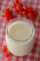 yogurt in a jar with red currant berries on a gingham tablecloth