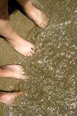 Feet of Two Girls in Sand at Beach with Water